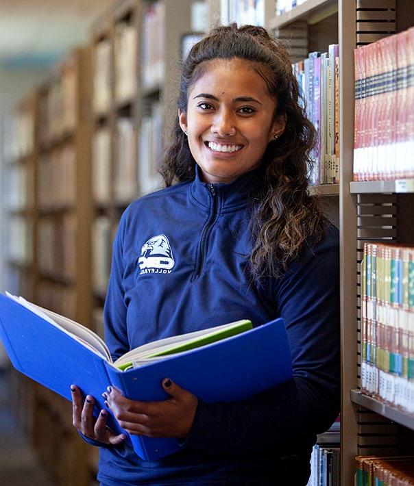 student standing with book in library